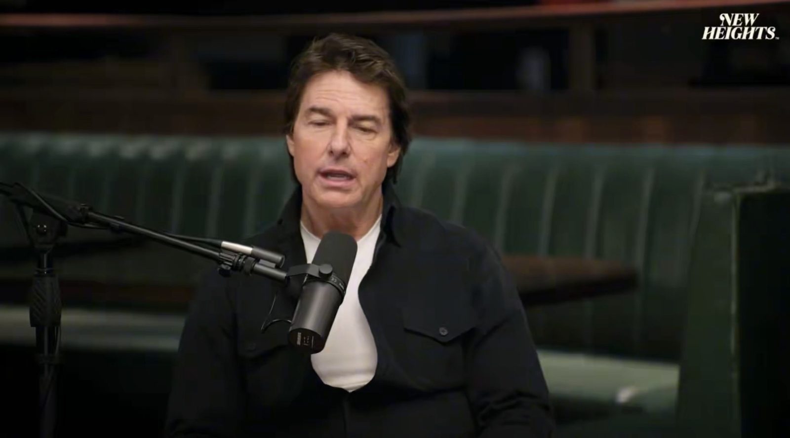 Tom Cruise speaking into a podcast microphone during his appearance on the New Heights podcast